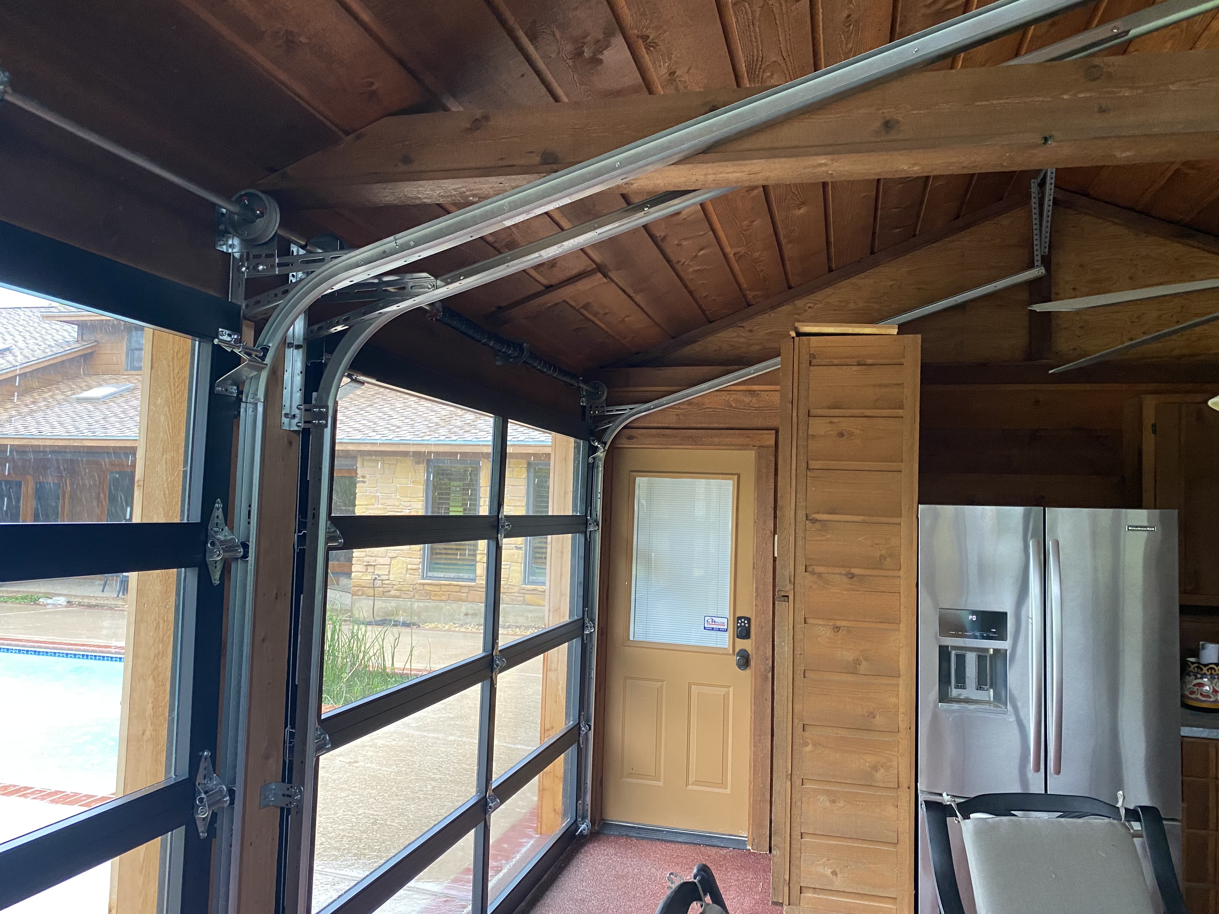 Interior view of full-view glass garage door open in cedar wood pool house with pool in background