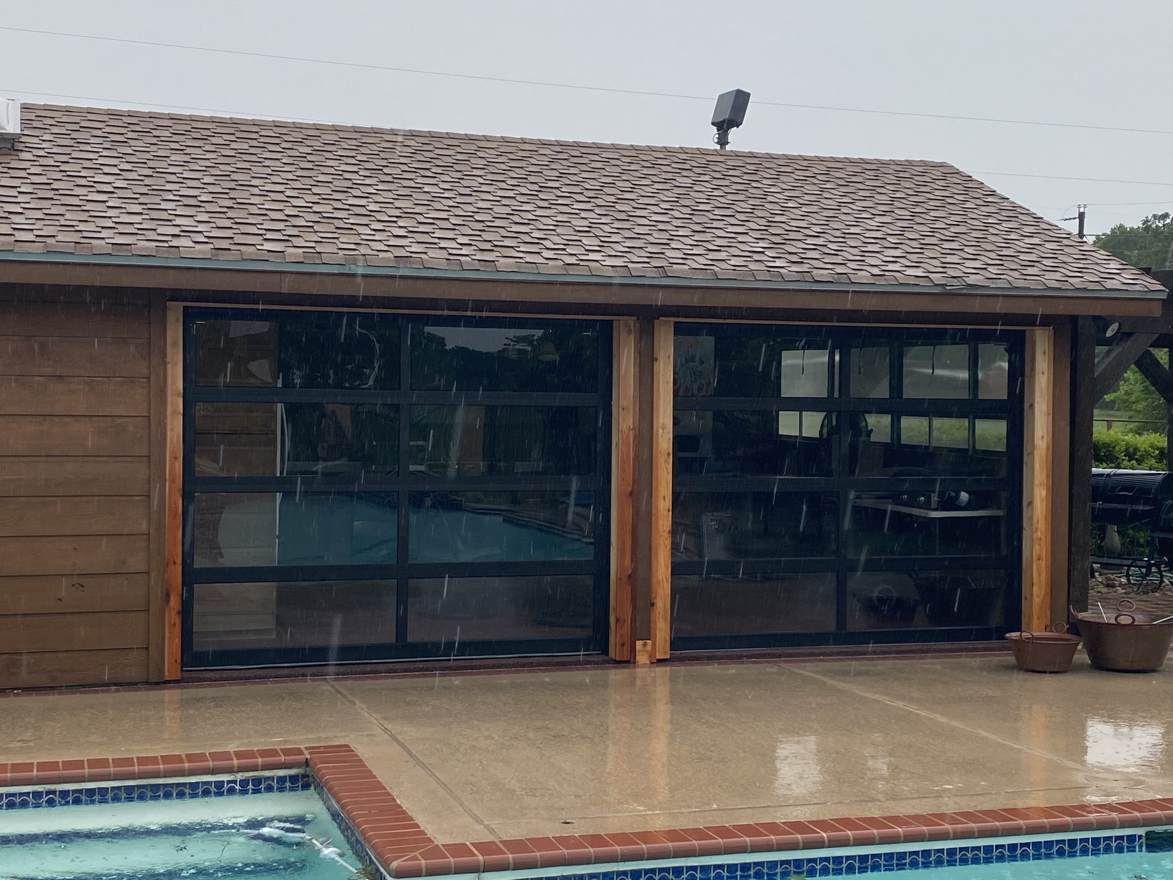 Two full-view glass garage doors on cedar post pool house, installed by Palousek Overhead Doors
