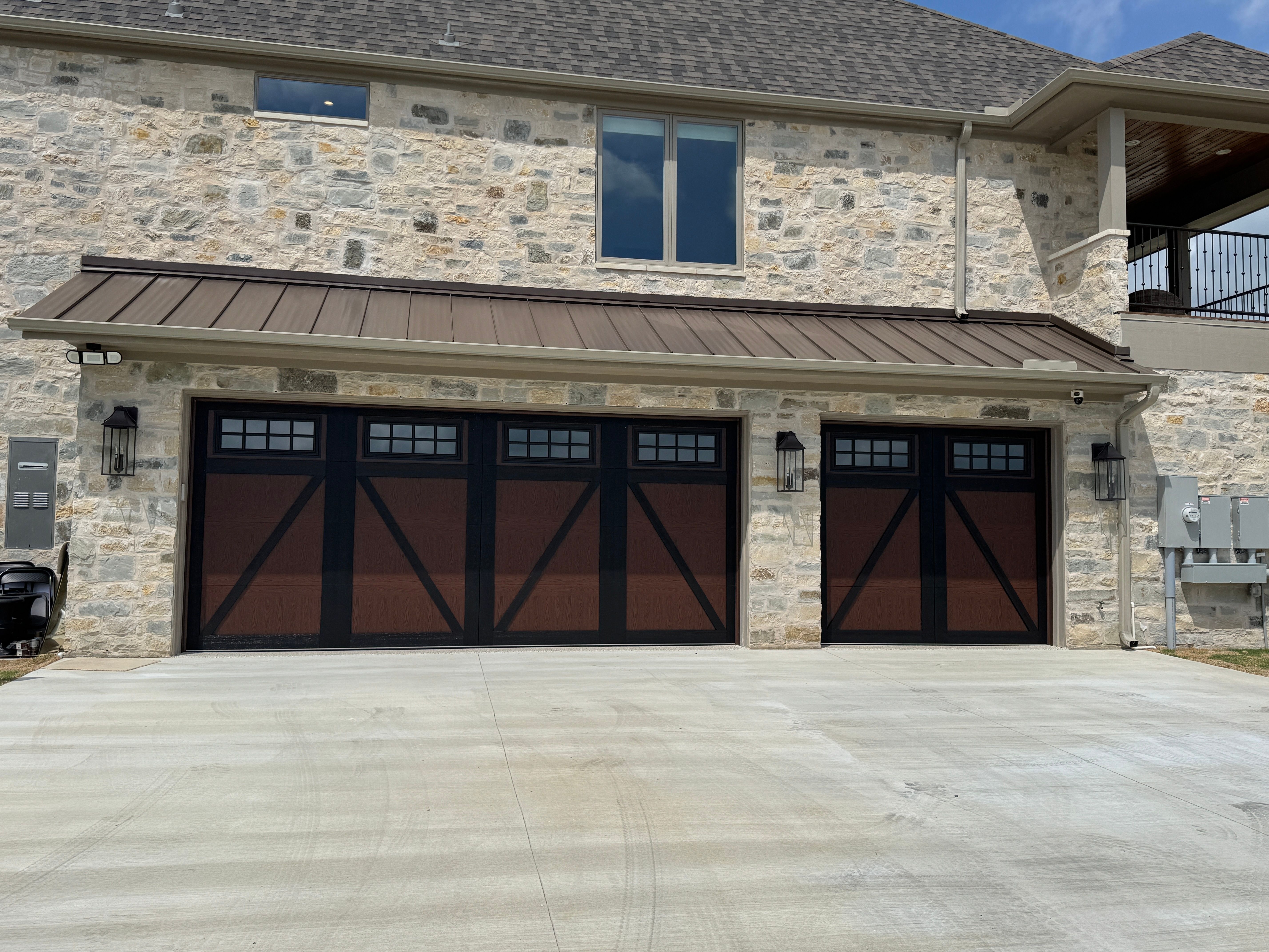 Dark carriage-style garage doors with black hardware and windows on limestone home in Temple, TX