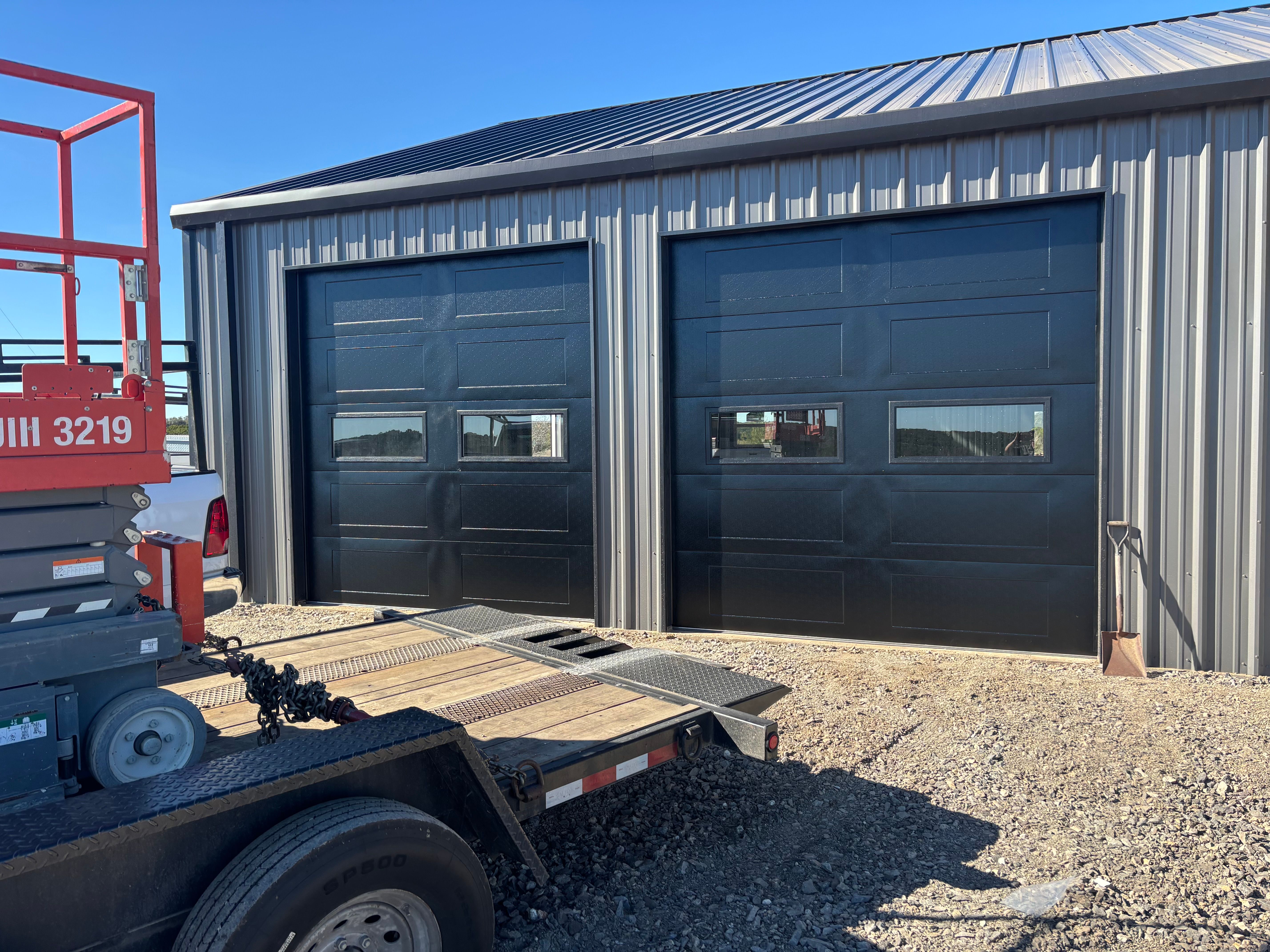 Two matte black panel garage doors with windows installed on gray metal commercial building in Texas