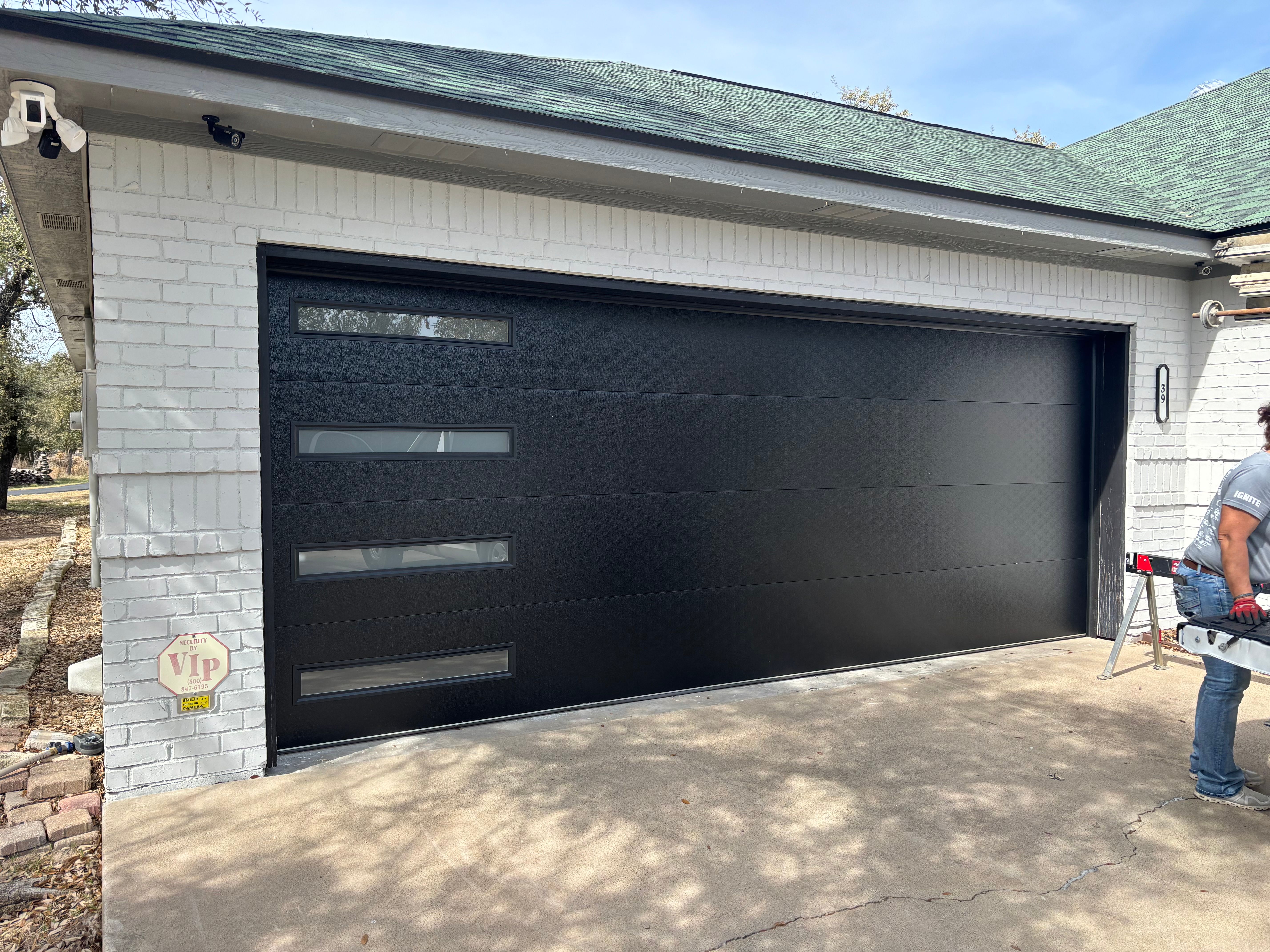 Modern black garage door with horizontal accent windows being installed by Palousek technician