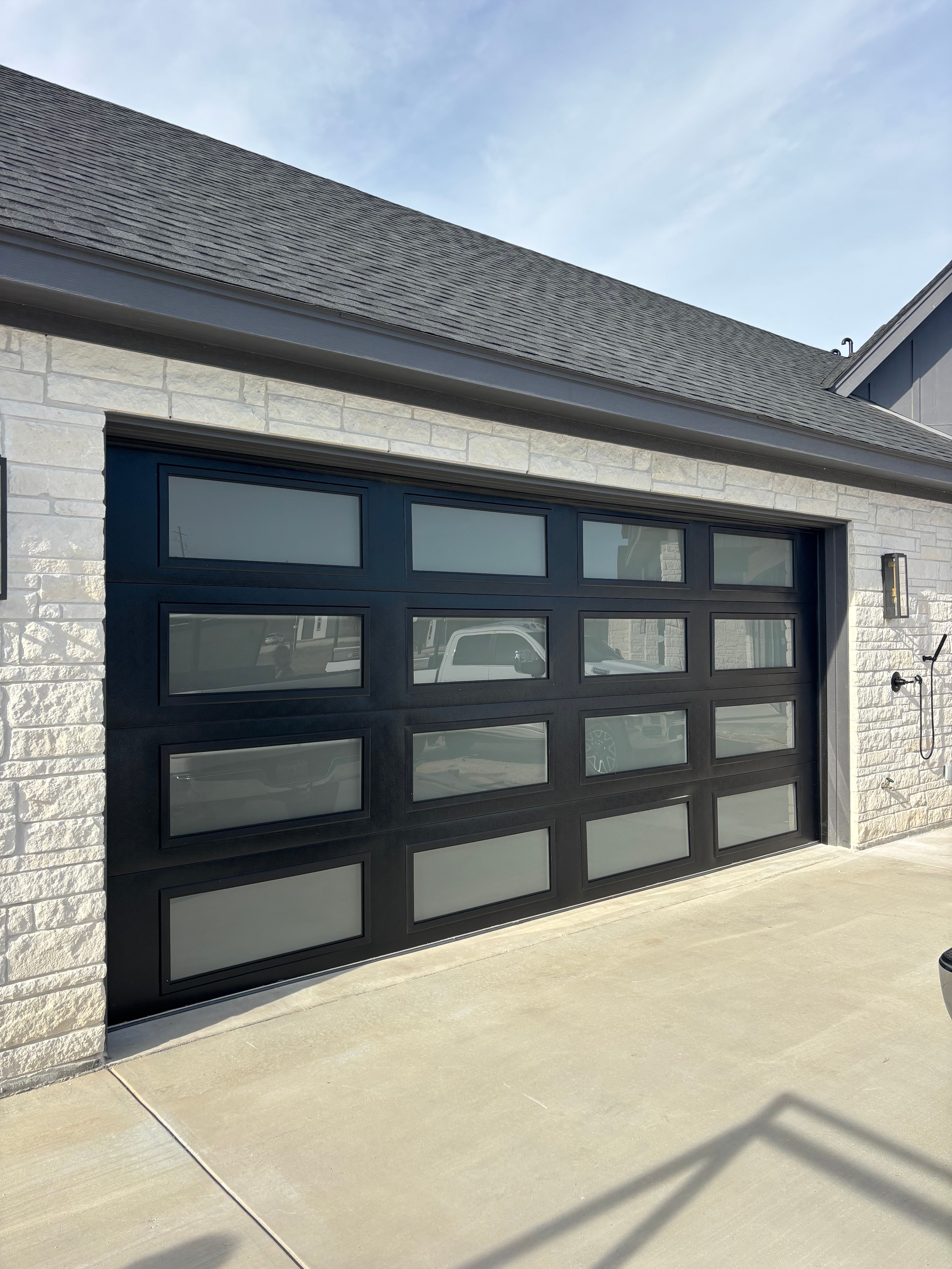 Black full-view glass panel garage door installed on white limestone home in Temple, TX