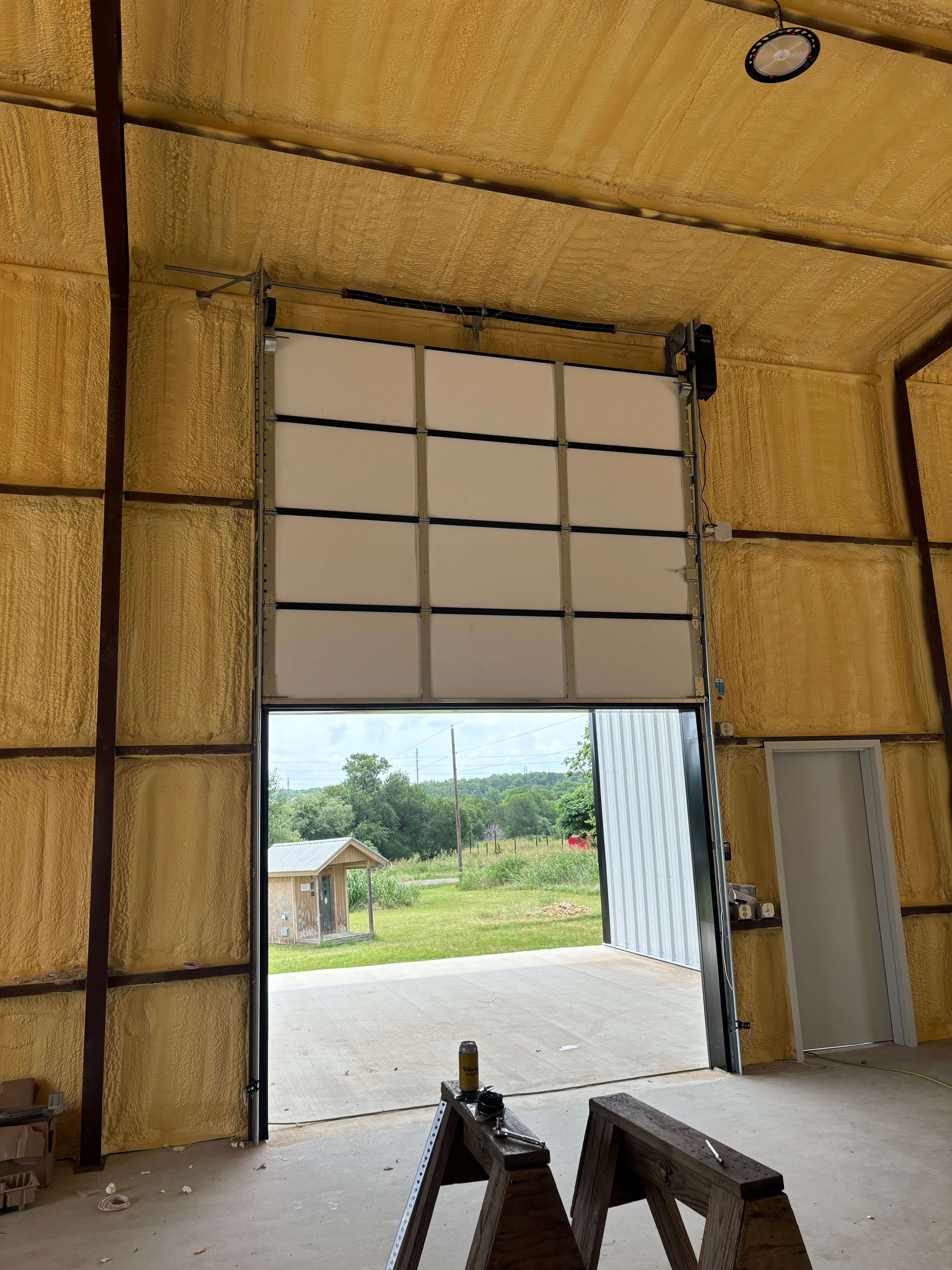 Large white insulated sectional overhead door installed in a spray-foam agricultural metal building in Central Texas by Palousek Overhead Doors