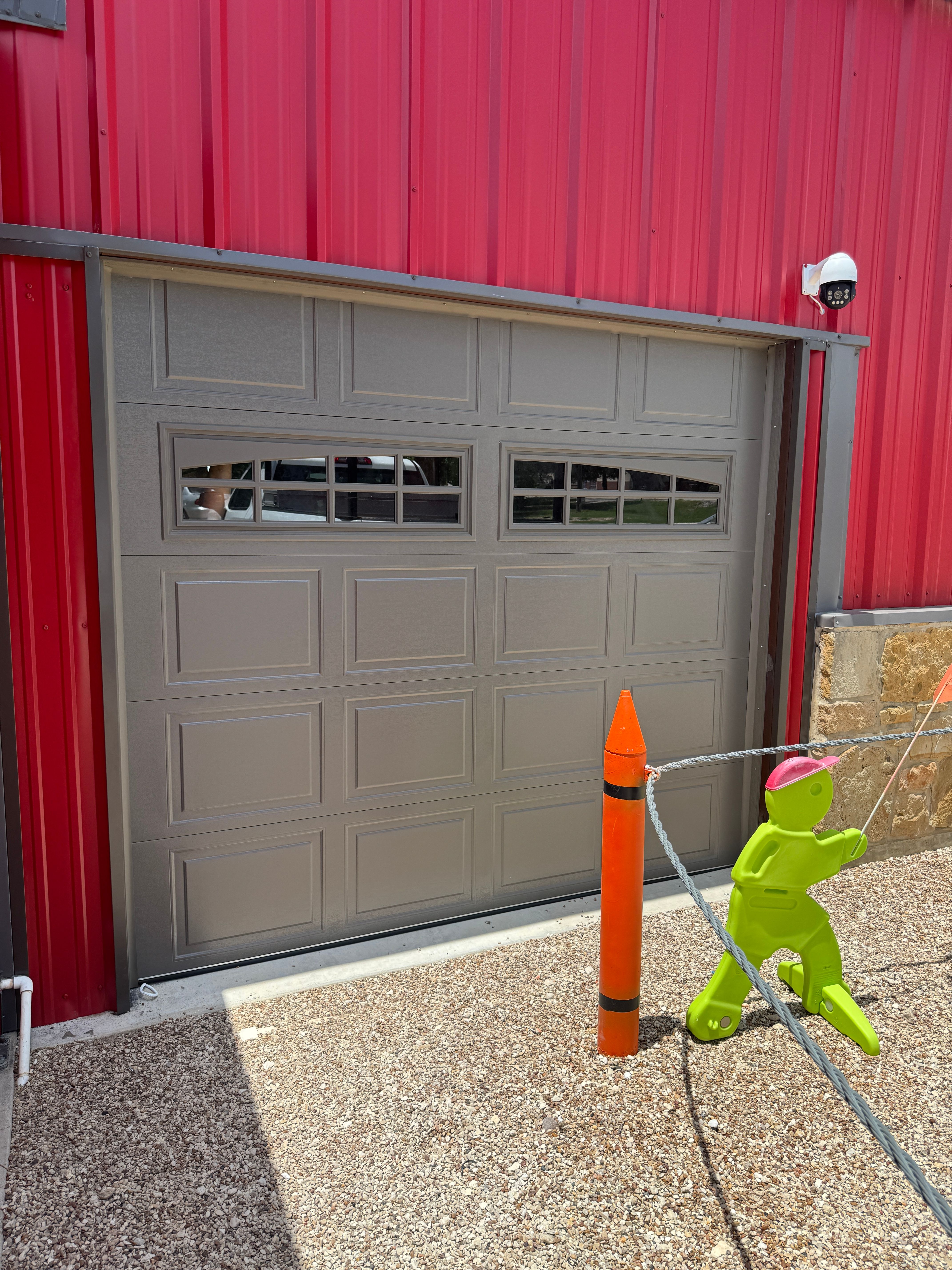 Gray raised-panel garage door with colonial window inserts installed on a red metal barndominium in Central Texas