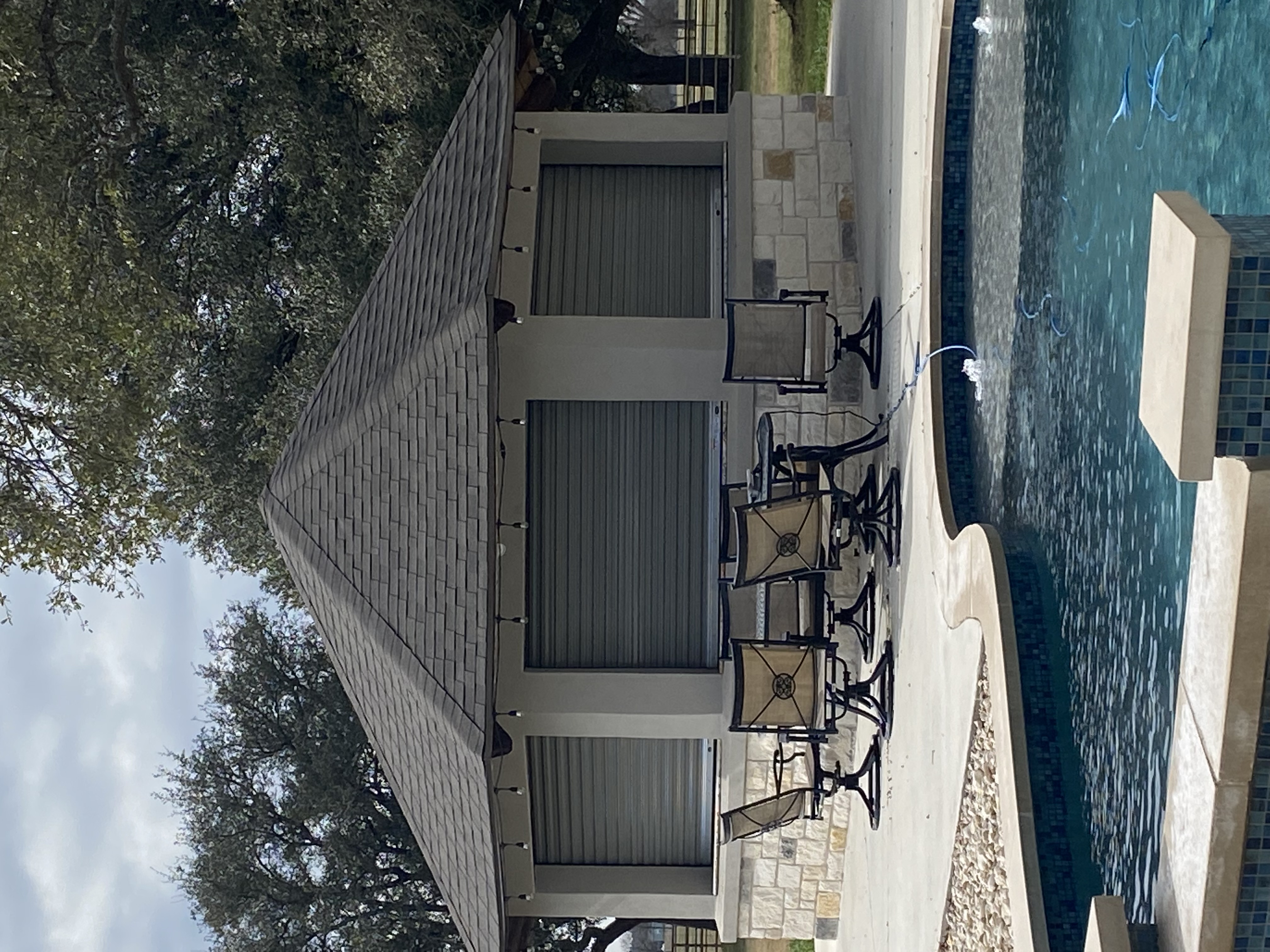 Three gray roll-up overhead doors installed on a Texas limestone outdoor pool pavilion bar area by Palousek Overhead Doors