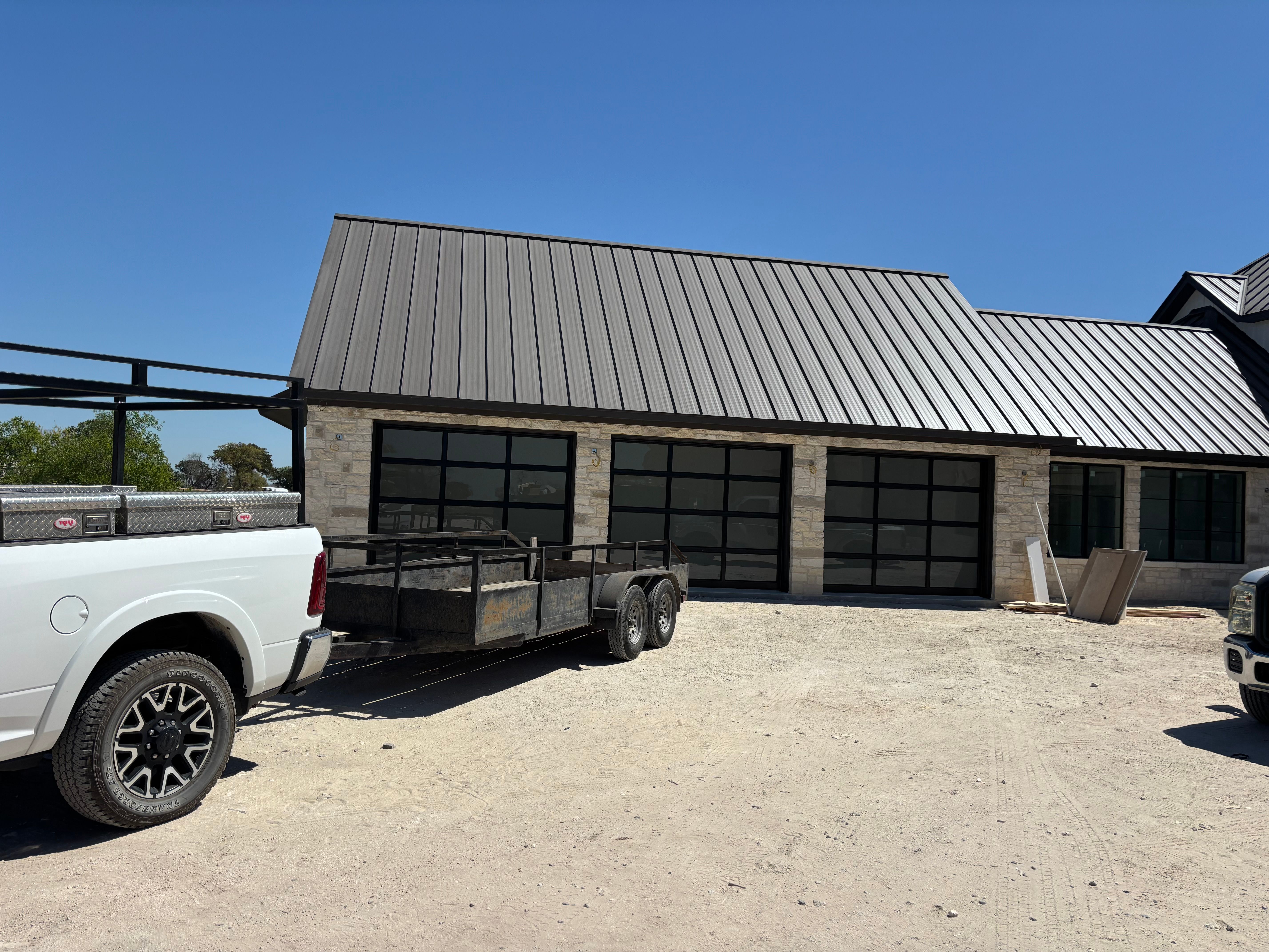 Palousek Overhead Doors service truck and trailer parked in front of new-construction limestone home with three full-view black-frame glass garage doors