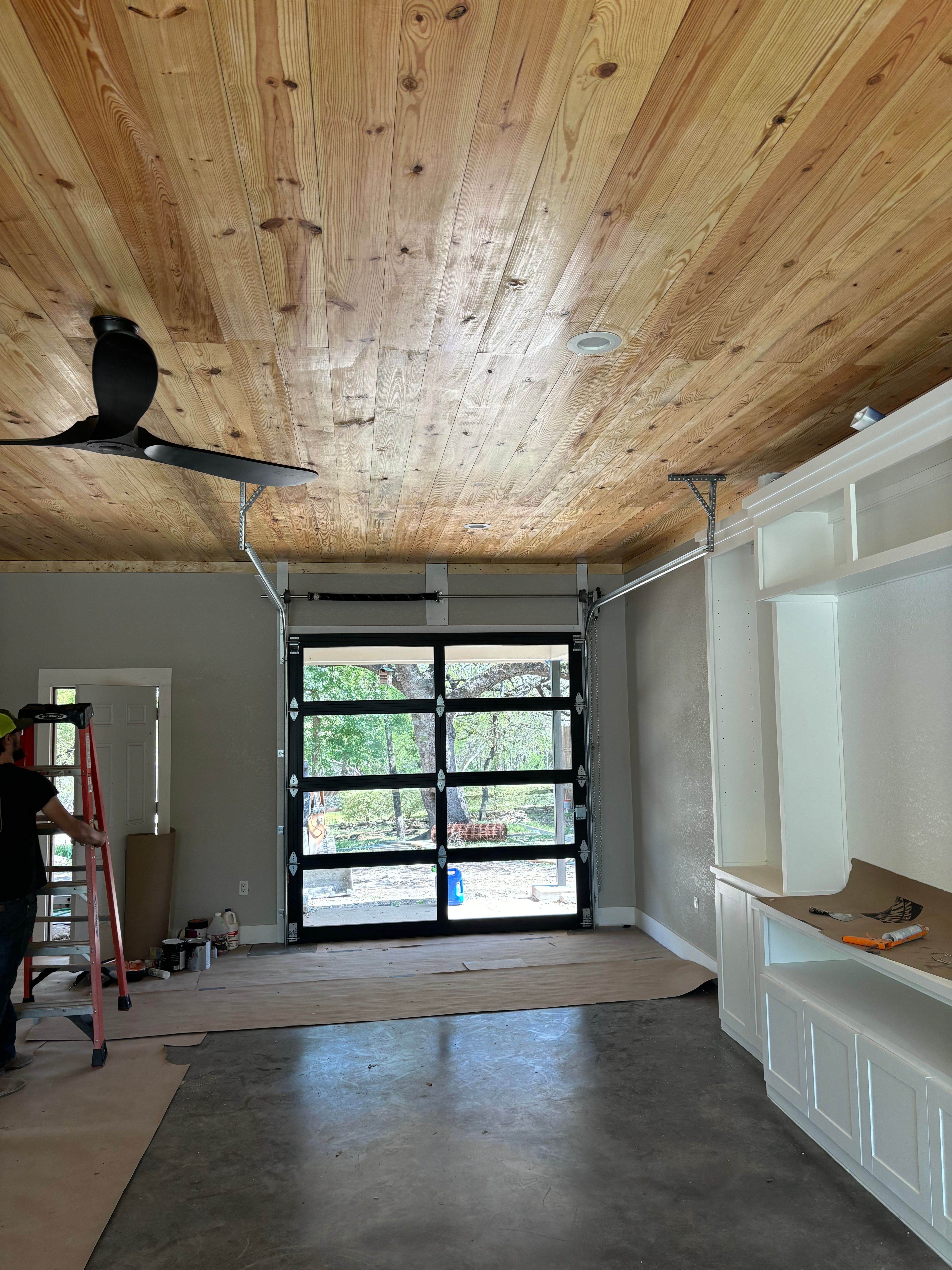 Palousek technician installing a full-view glass garage door in a custom home with natural cedar plank ceiling in Central Texas