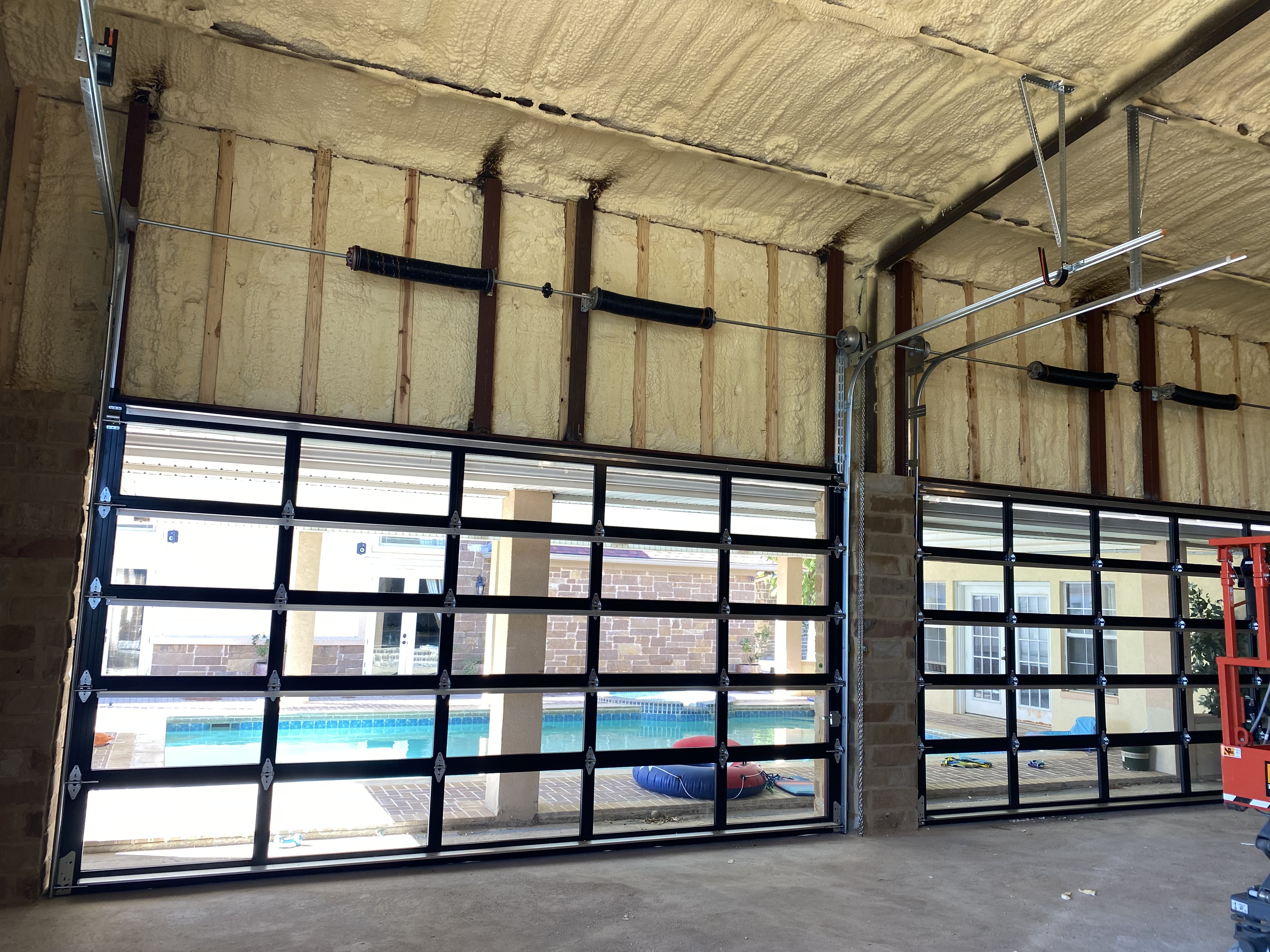 Interior of spray-foam insulated pool enclosure with two large full-view glass overhead doors installed by Palousek Overhead Doors, Central Texas