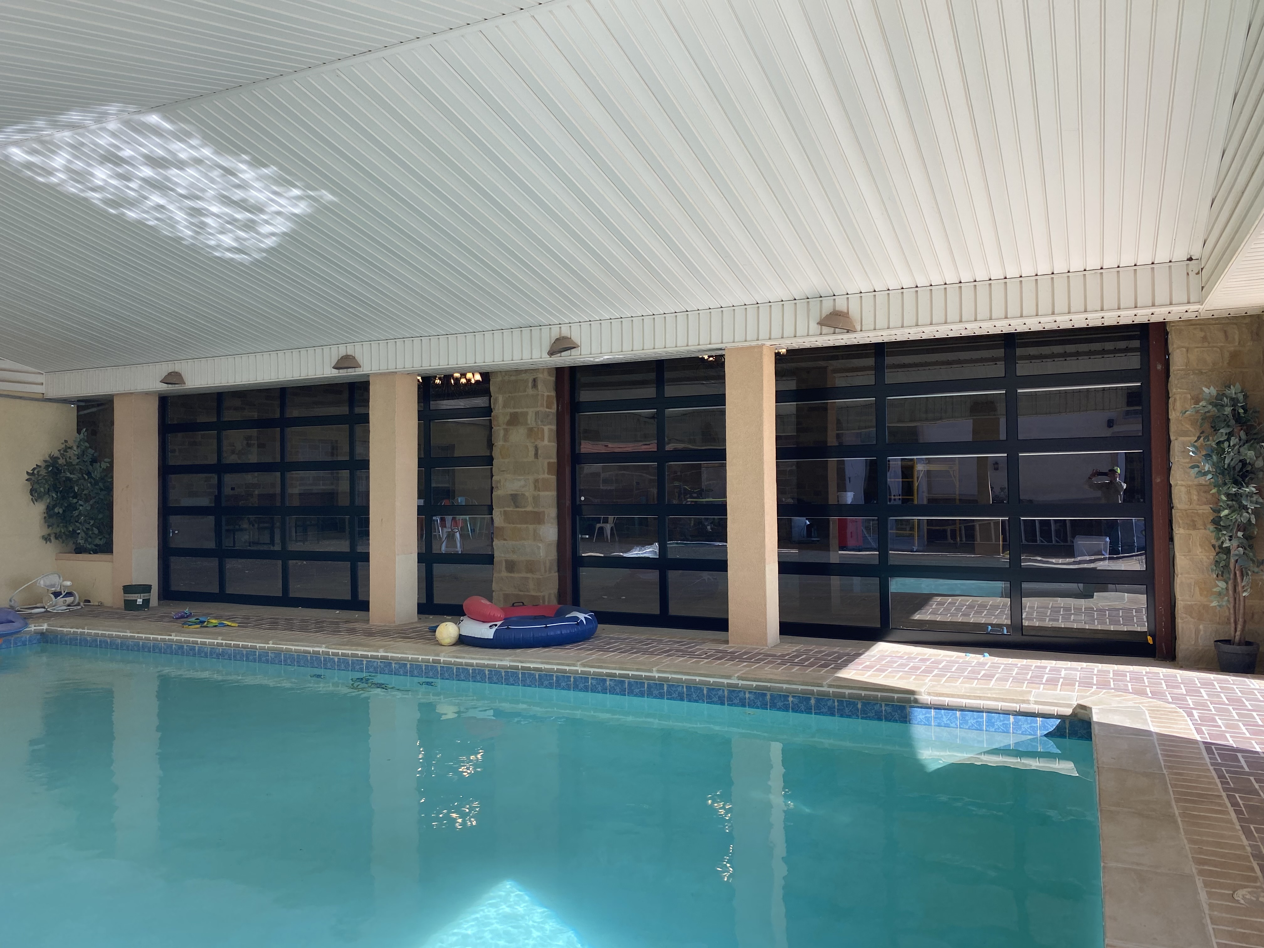 Indoor swimming pool with four full-view glass overhead doors along the wall, stone columns, installed by Palousek Overhead Doors